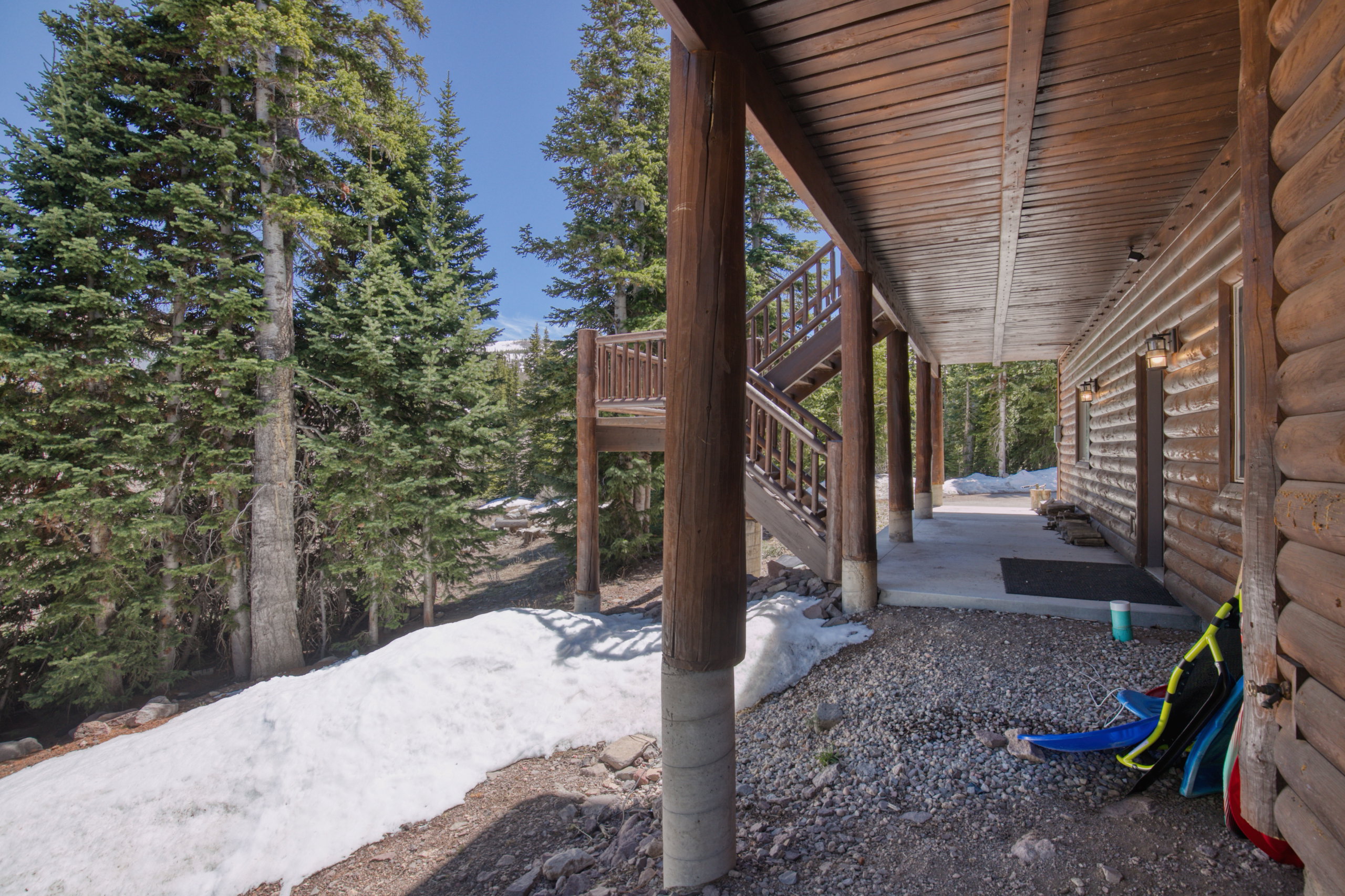 Exterior log cabin siding with an expansive covered porch, featuring a wood-plank ceiling and exposed support beams