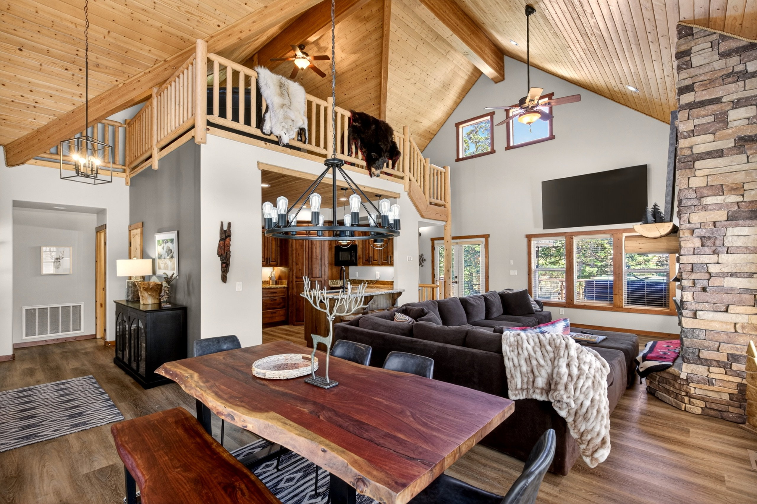 Open-concept living area featuring high vaulted wood-paneled ceilings, a stone fireplace, and wood-finish flooring