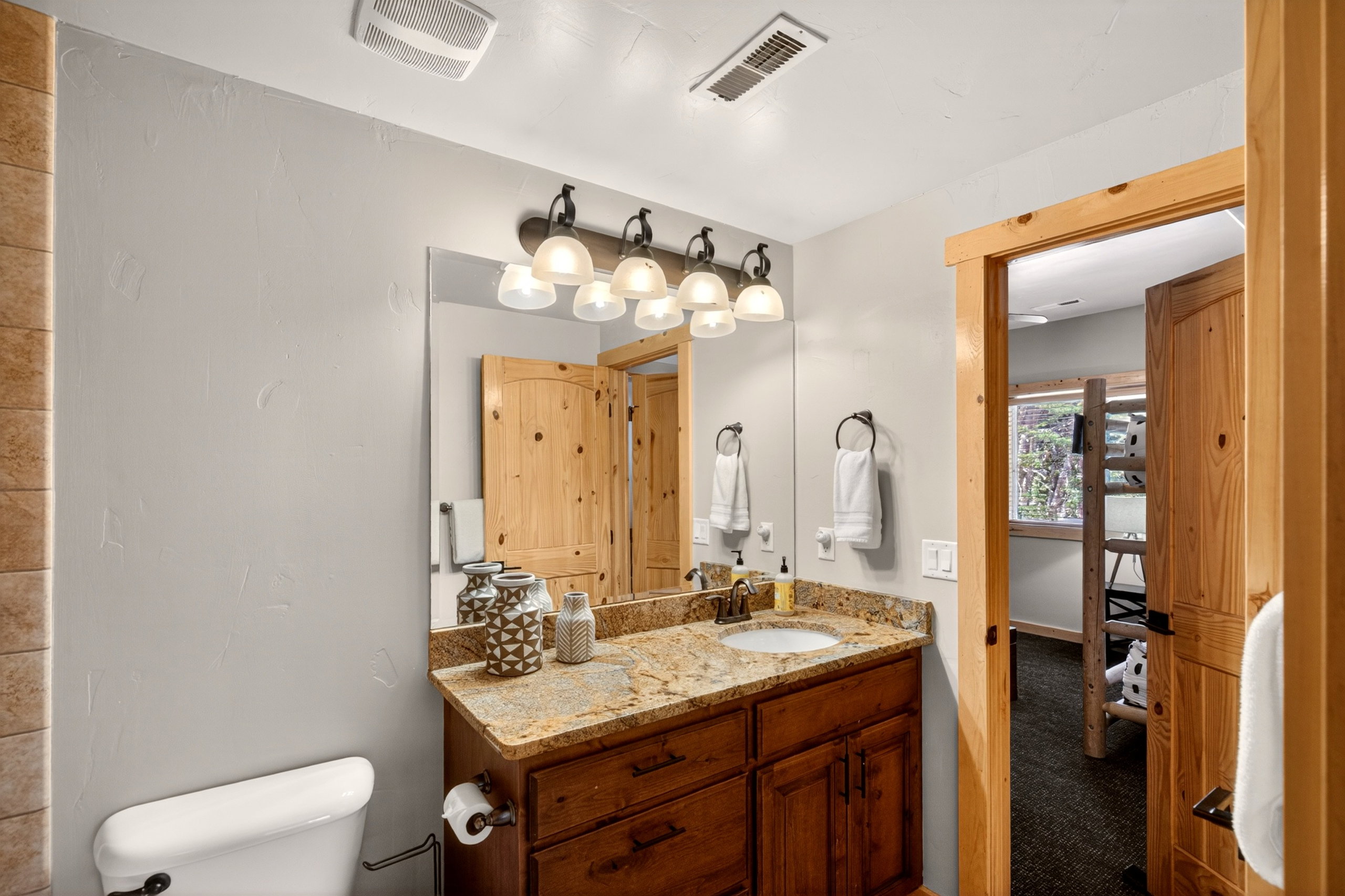 Bathroom featuring a dark wood vanity with a light-colored stone countertop, an undermount sink, and a four-light fixture
