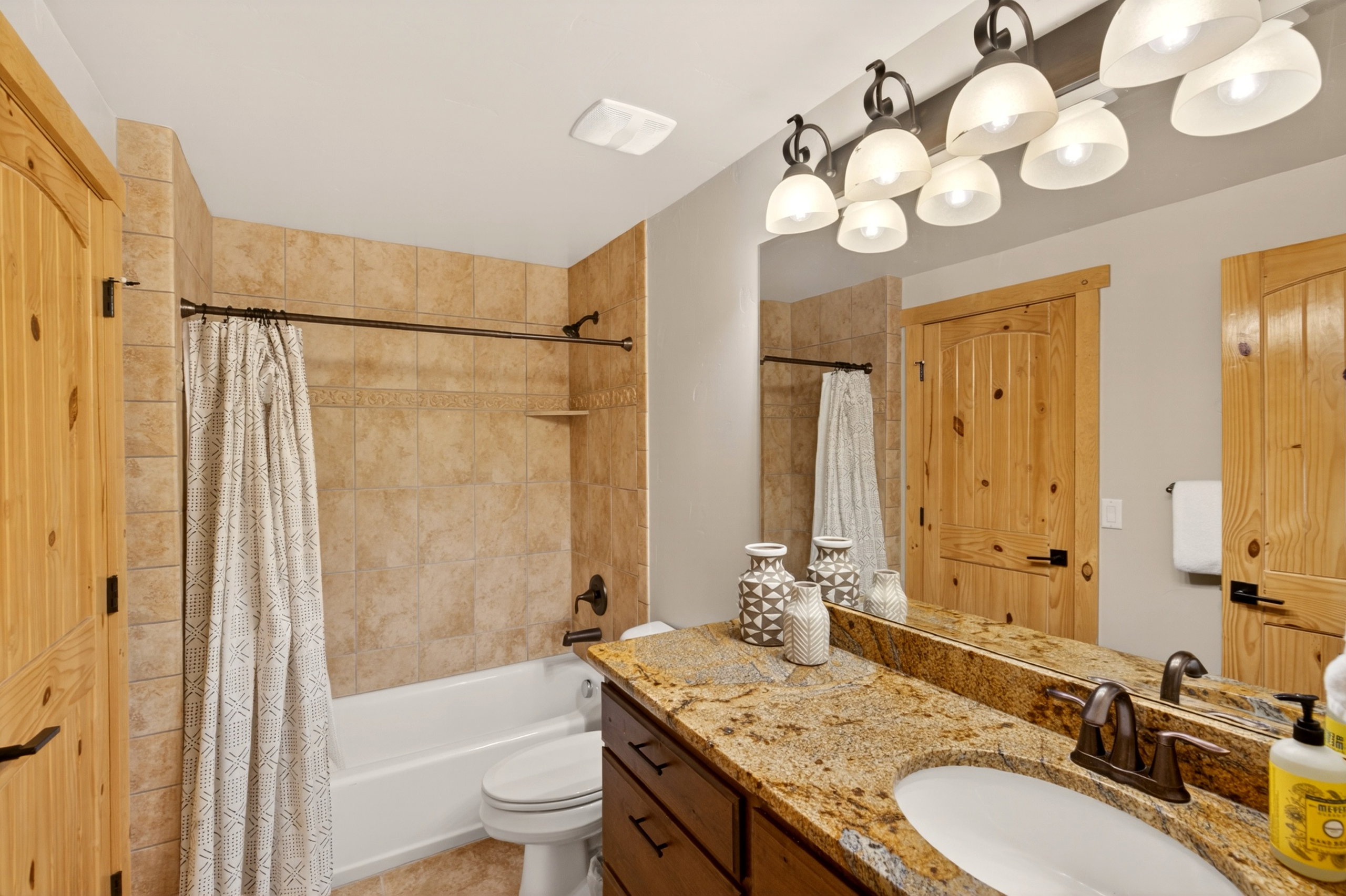 Bathroom featuring a granite-finish countertop, wood-finish cabinetry, drop-in sink with bronze-finish faucet, and a large vanity mirror