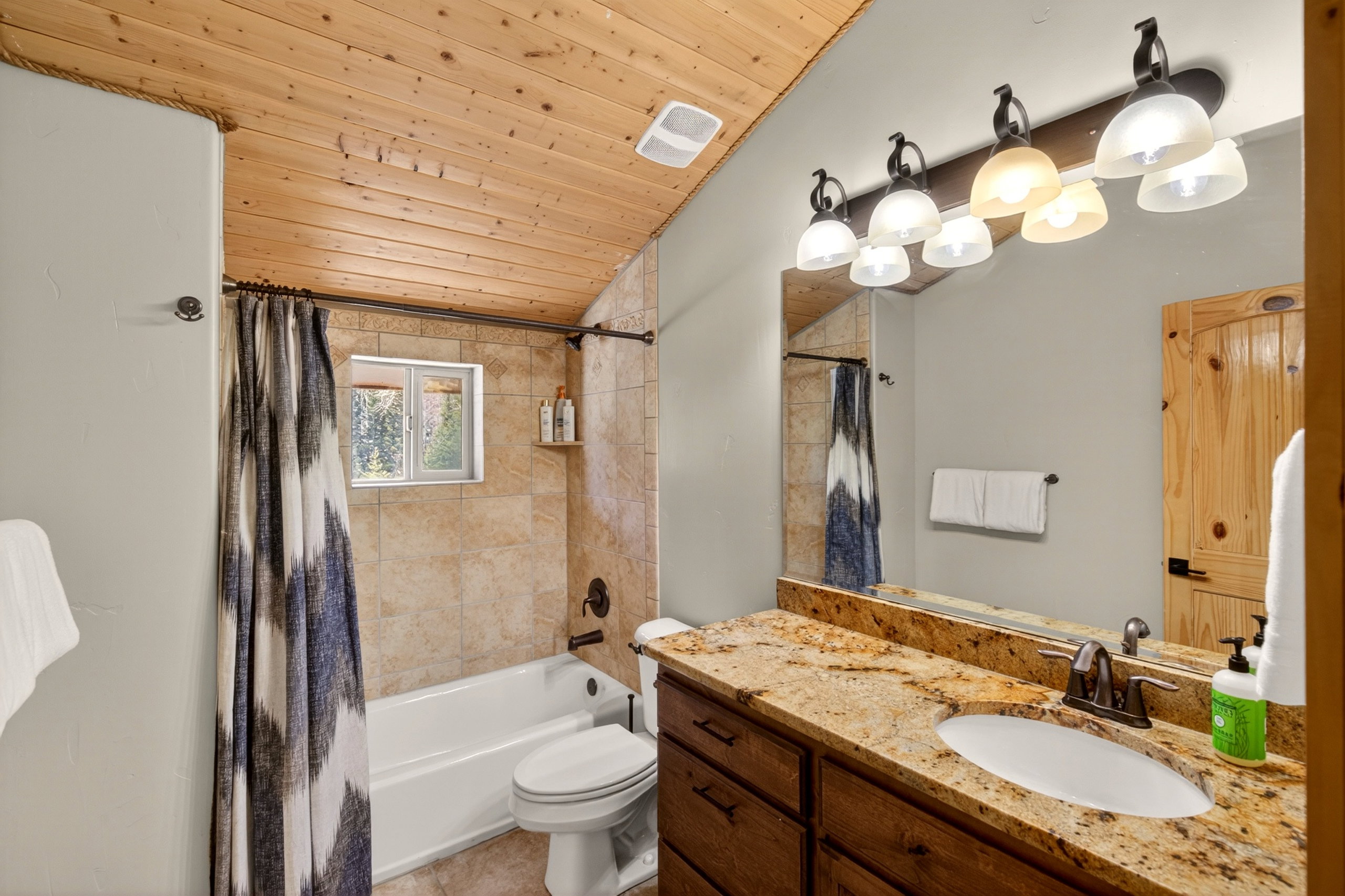 Bathroom featuring a wood-planked vaulted ceiling, a vanity with a granite countertop and an undermount sink, and a tiled shower-tub combination with a window