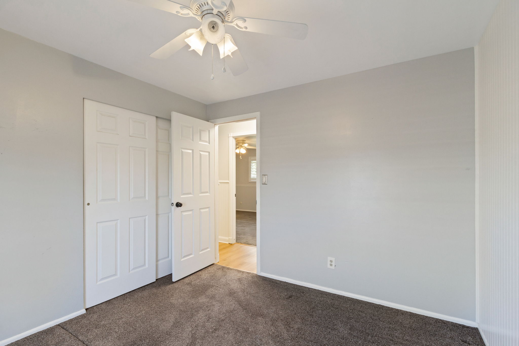 Carpeted room with a ceiling fan light fixture, white six-panel bifold closet doors, and light gray painted walls
