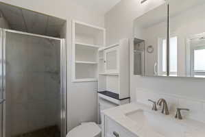 Bathroom featuring a glass-enclosed shower with tile surround, a built-in shelving unit, and a vanity with an undermount sink and brushed nickel faucet