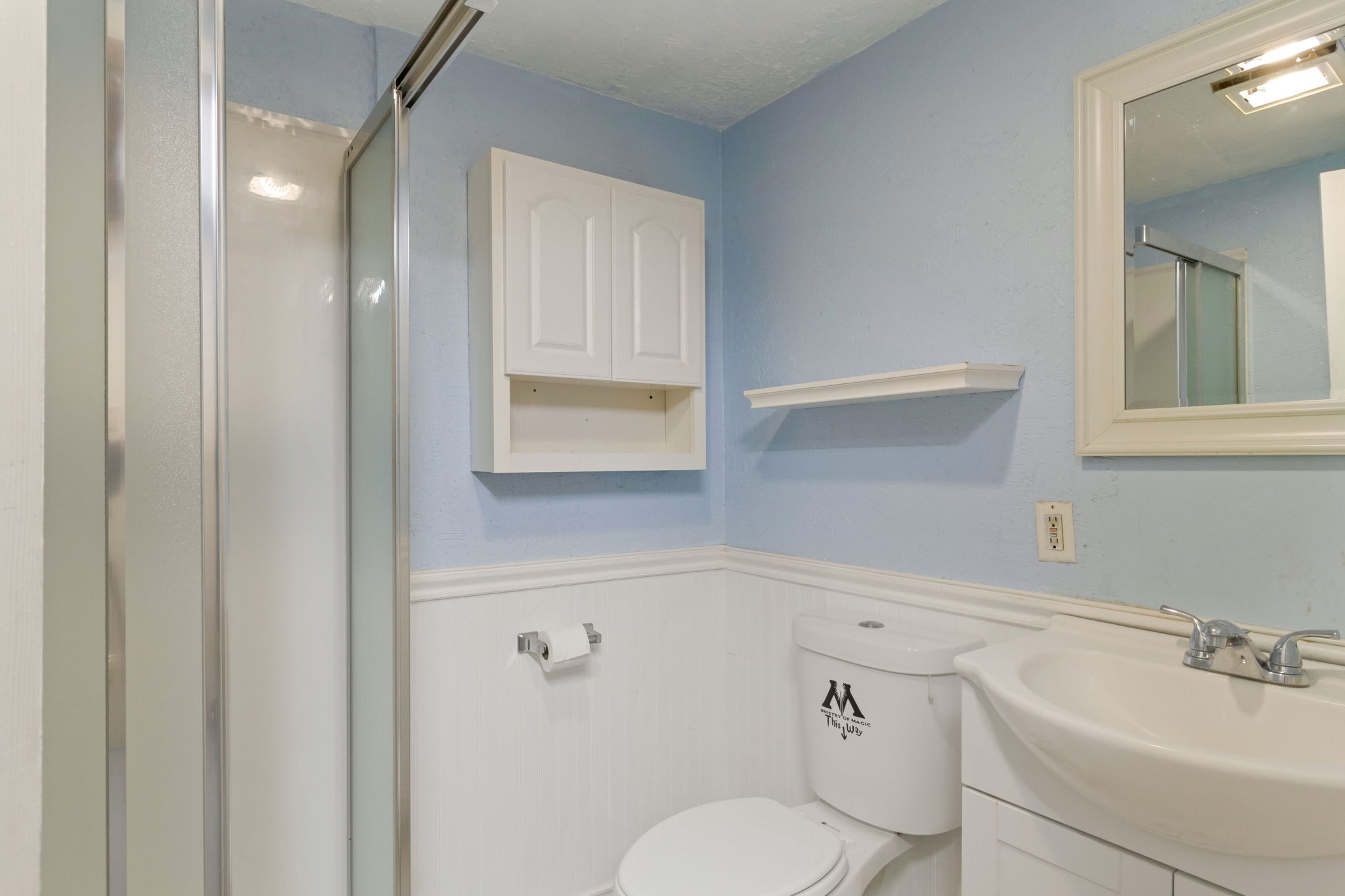 Bathroom featuring a glass-enclosed shower, wall-mounted storage cabinet, white vanity with integrated sink, and framed mirror