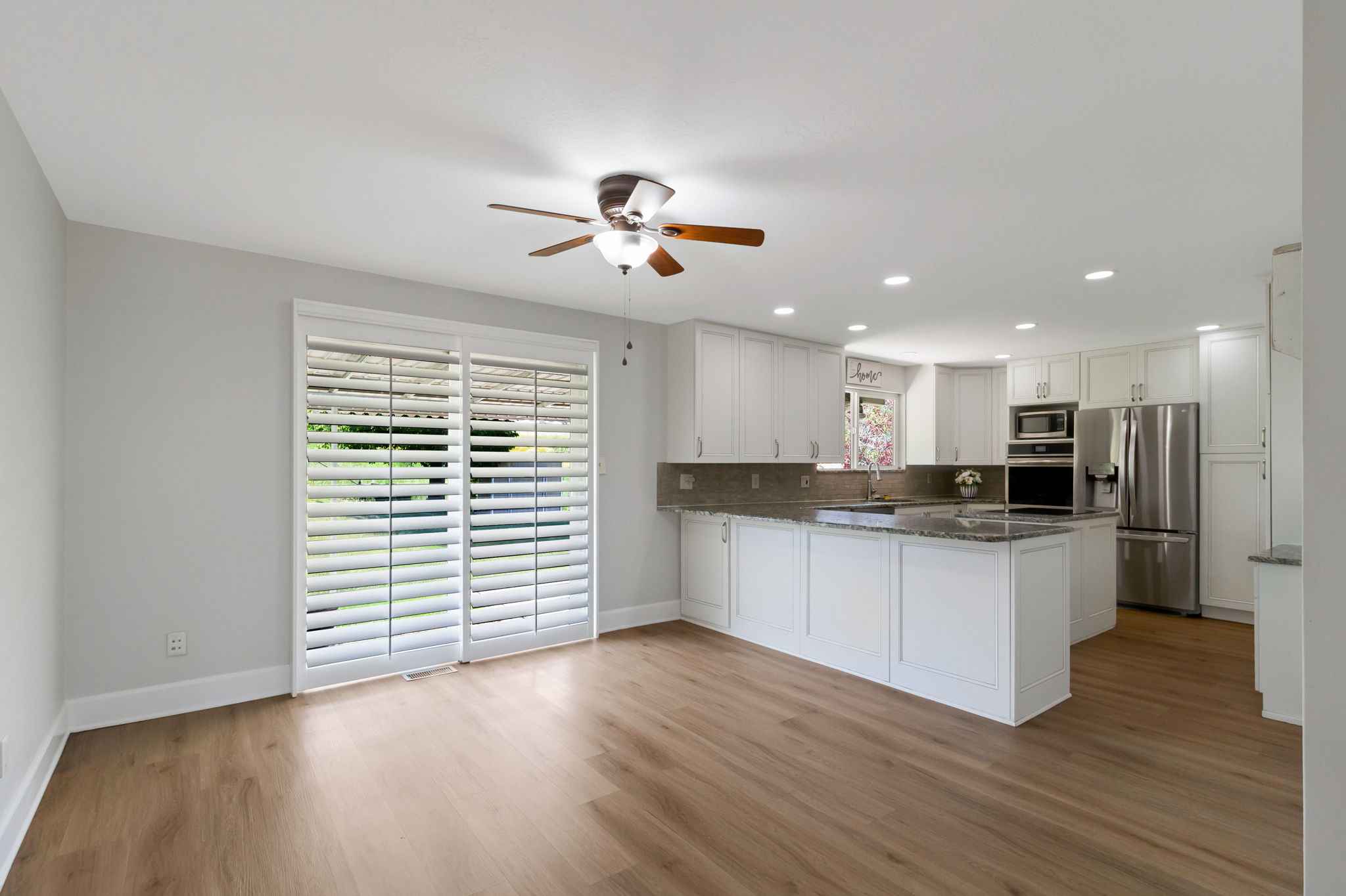 Open-concept living area featuring wood-look flooring, a contemporary ceiling fan, and sliding glass doors with white plantation shutters