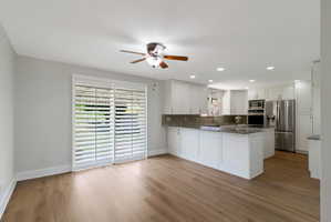 Open-concept living area featuring wood-look flooring, a contemporary ceiling fan, and sliding glass doors with white plantation shutters