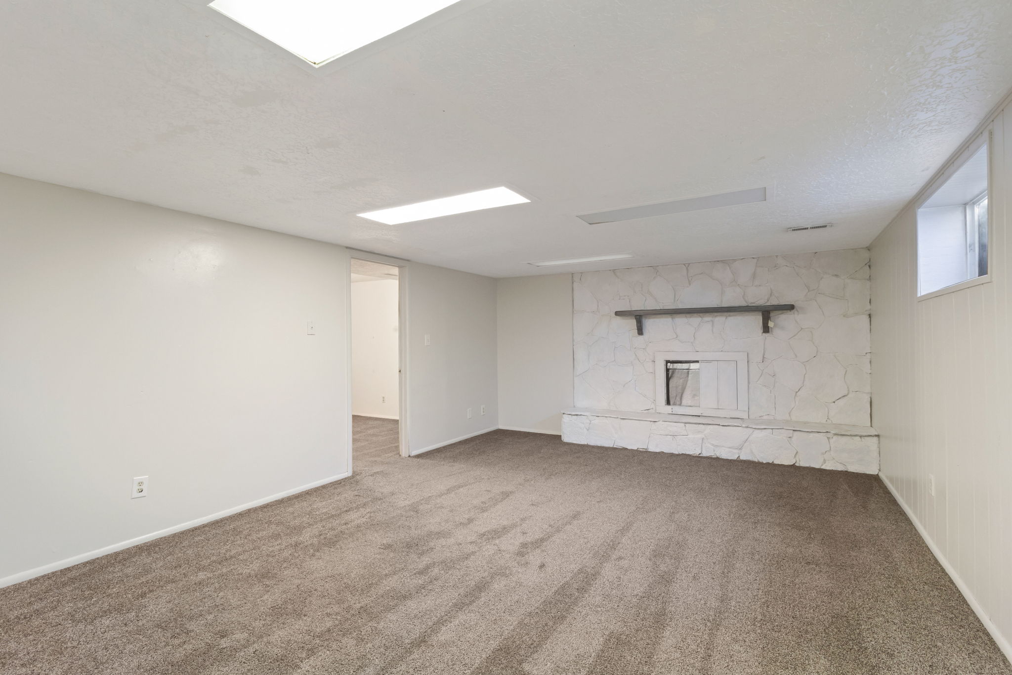 Spacious room featuring a stone-clad fireplace with a mantel, carpeted flooring, white walls, and recessed lighting