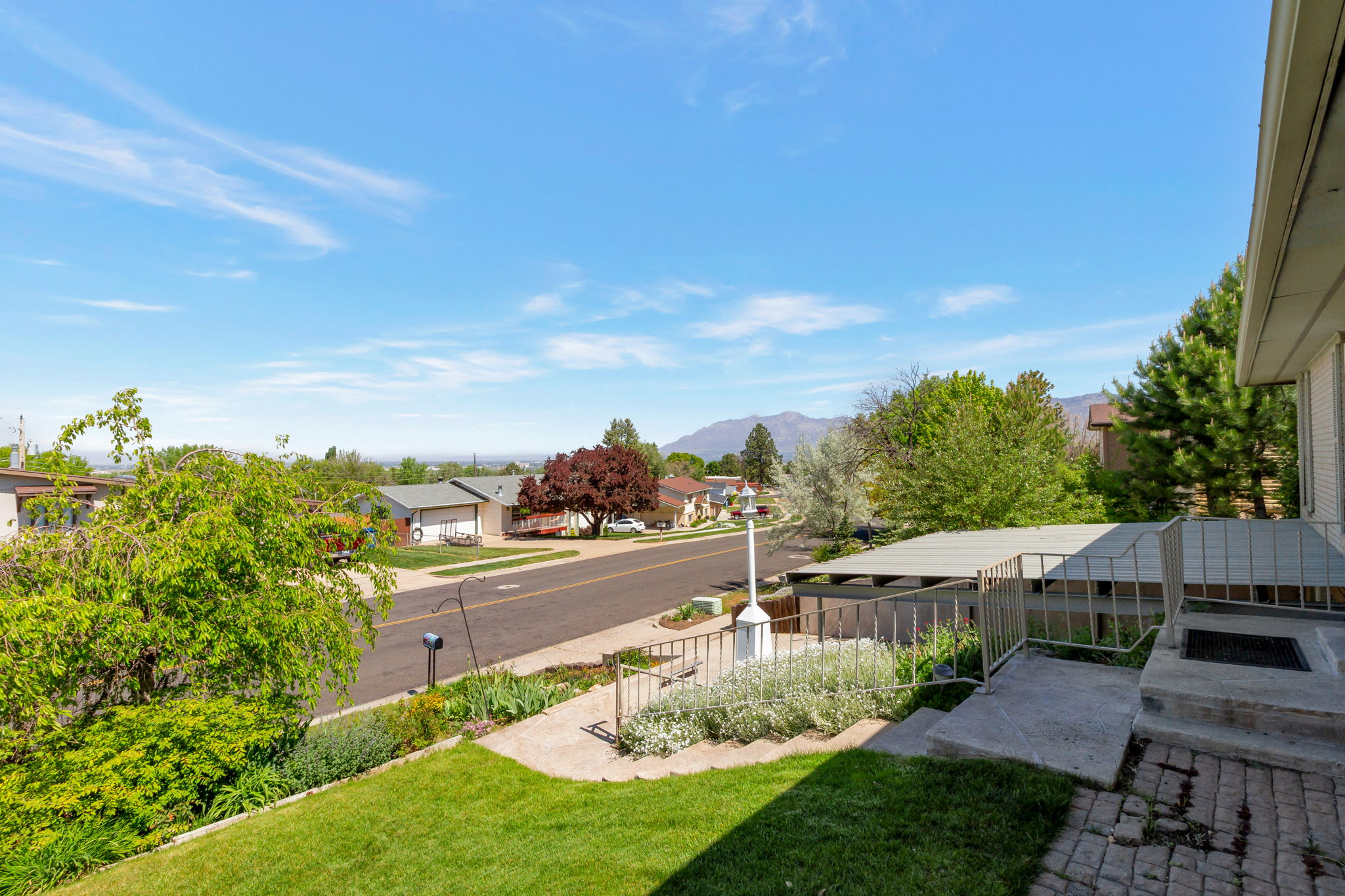 Front entrance with brick paver landing, metal railing, and covered carport