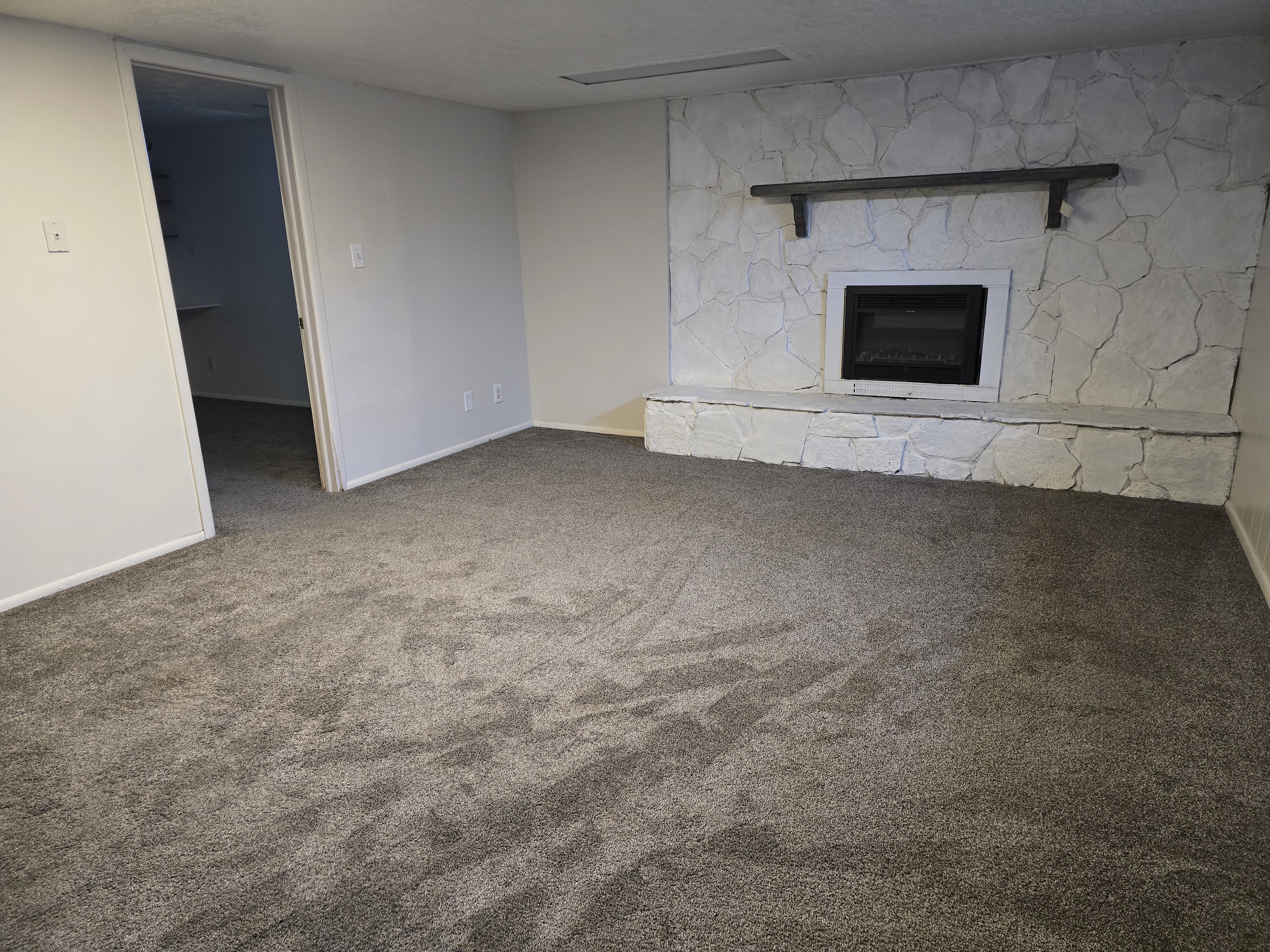 Living area featuring a stone-clad fireplace with a dark mantel shelf, light gray walls, plush gray carpeting, and white trim
