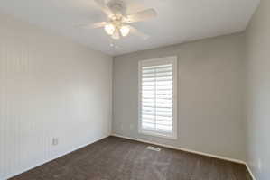 Neutral-toned room featuring a white ceiling fan with integrated lighting, a window with plantation shutters, vertical plank wall paneling, and carpet flooring