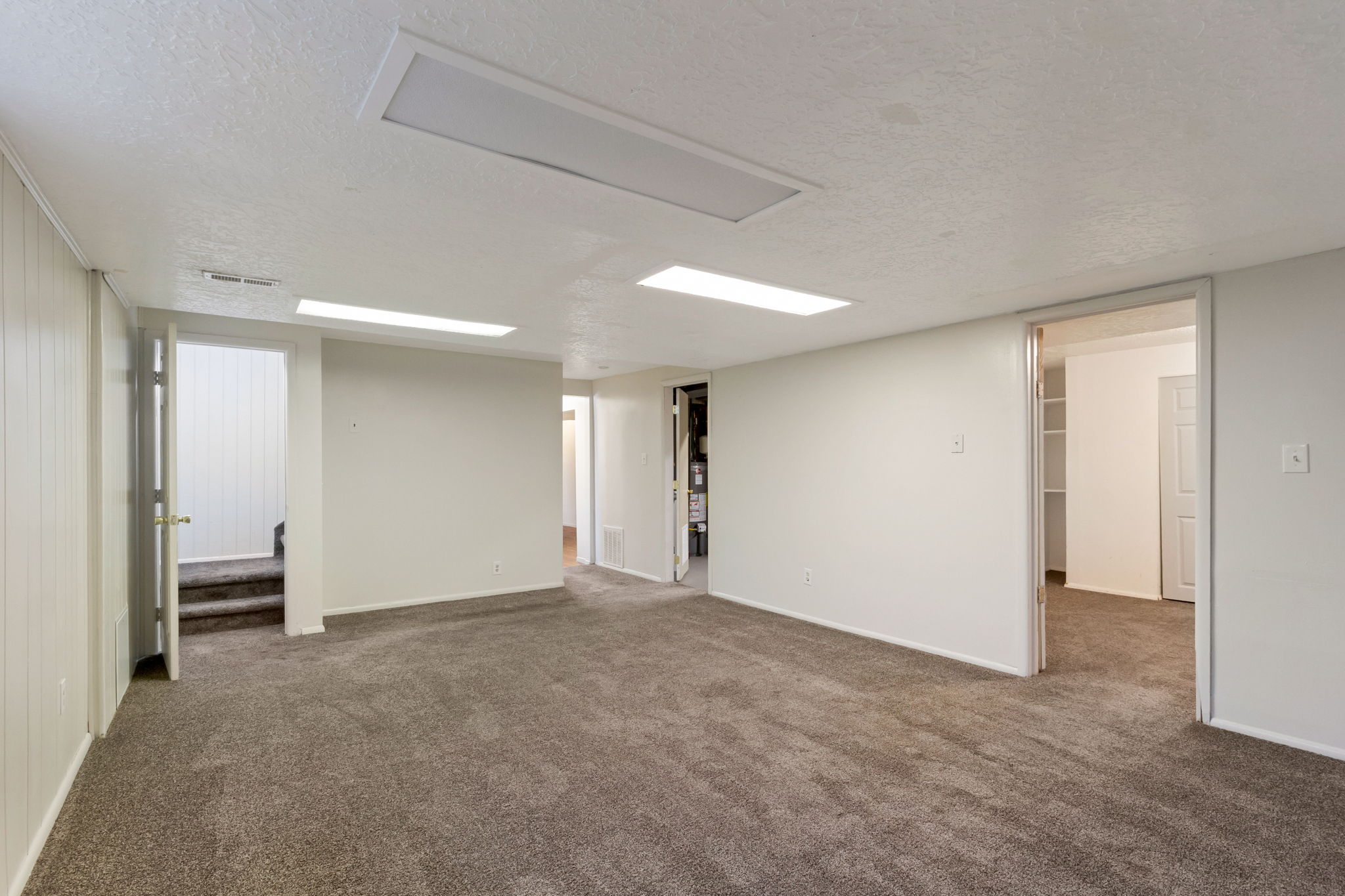 Spacious room featuring neutral carpeting, white painted walls, recessed lighting, and multiple doorways