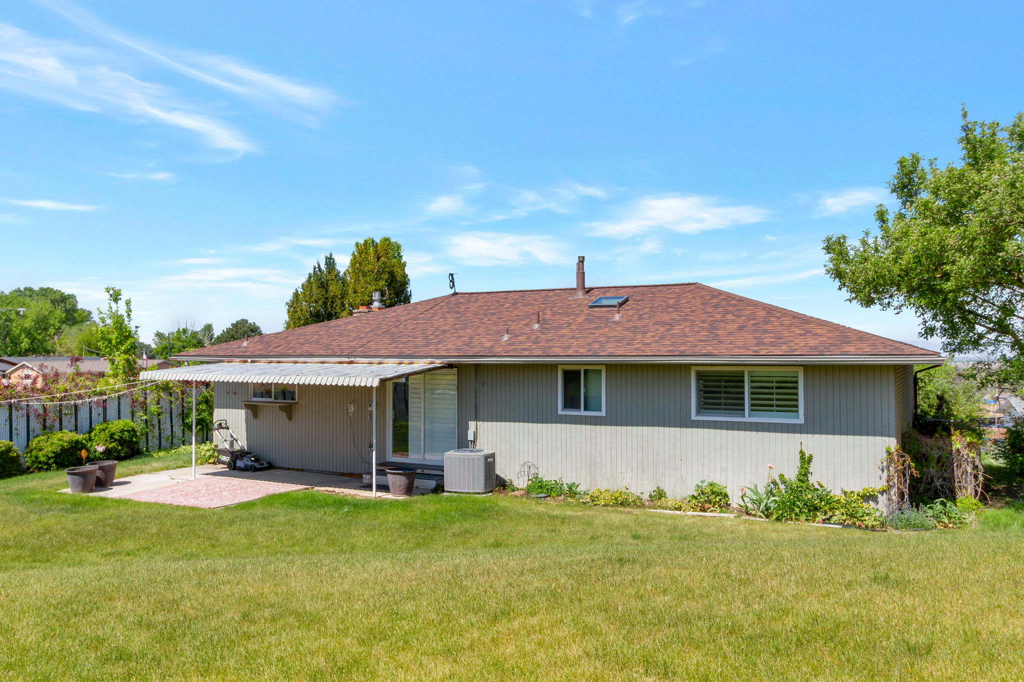 Expansive backyard featuring a manicured lawn, a covered patio area with a concrete surface, and a brown shingle roof