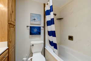 Full bathroom featuring a white bathtub/shower combination with a single shower head, a standard white toilet, and light wood-finish cabinetry