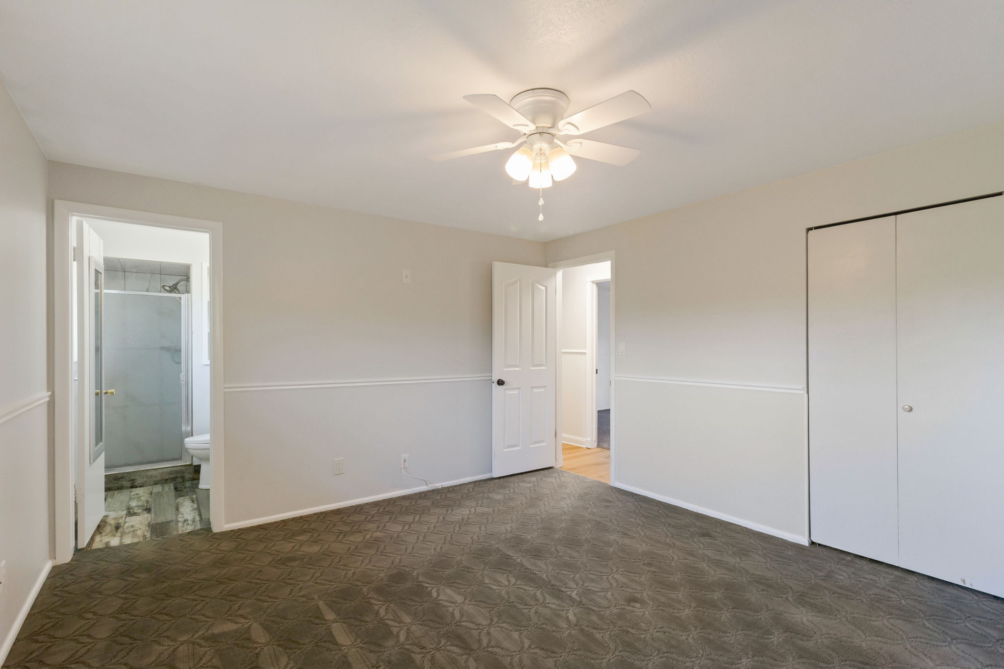Carpeted room featuring a ceiling fan with light fixture, chair rail molding, and panel doors