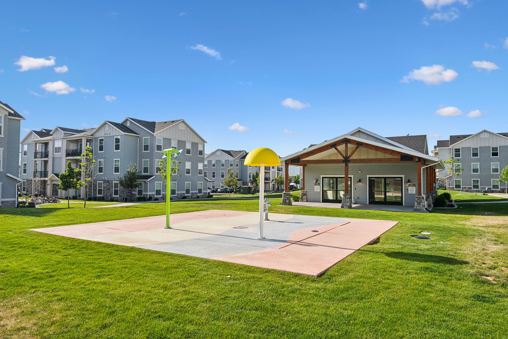 Community recreation space featuring a splash pad, a pavilion with exposed timber framing, and expansive green areas