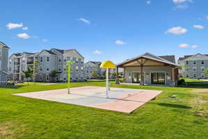 Community recreation space featuring a splash pad, a pavilion with exposed timber framing, and expansive green areas