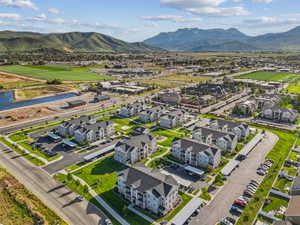 Aerial perspective of a multi-building residential community featuring covered parking structures, manicured green spaces, and a nearby pond