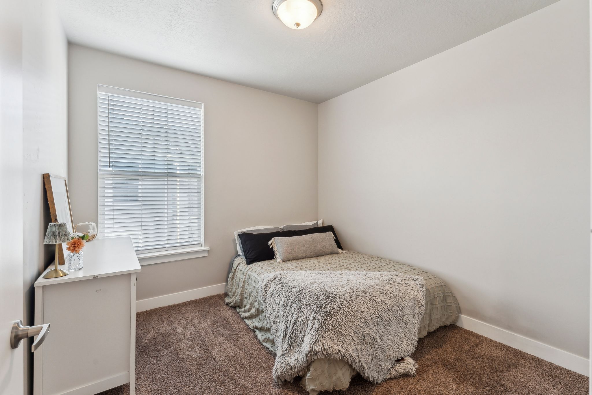 Carpeted room featuring light neutral wall paint, a single window with blinds, and a flush-mount ceiling light fixture