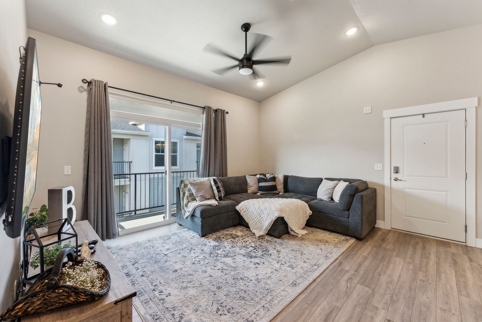 Vaulted ceilings featuring recessed lighting and a ceiling fan, sliding glass door with balcony access, wood-finish flooring, and a modern panel door