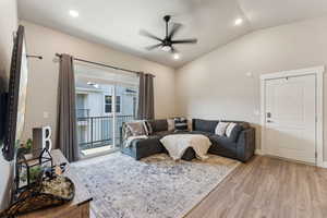 Vaulted ceilings featuring recessed lighting and a ceiling fan, sliding glass door with balcony access, wood-finish flooring, and a modern panel door