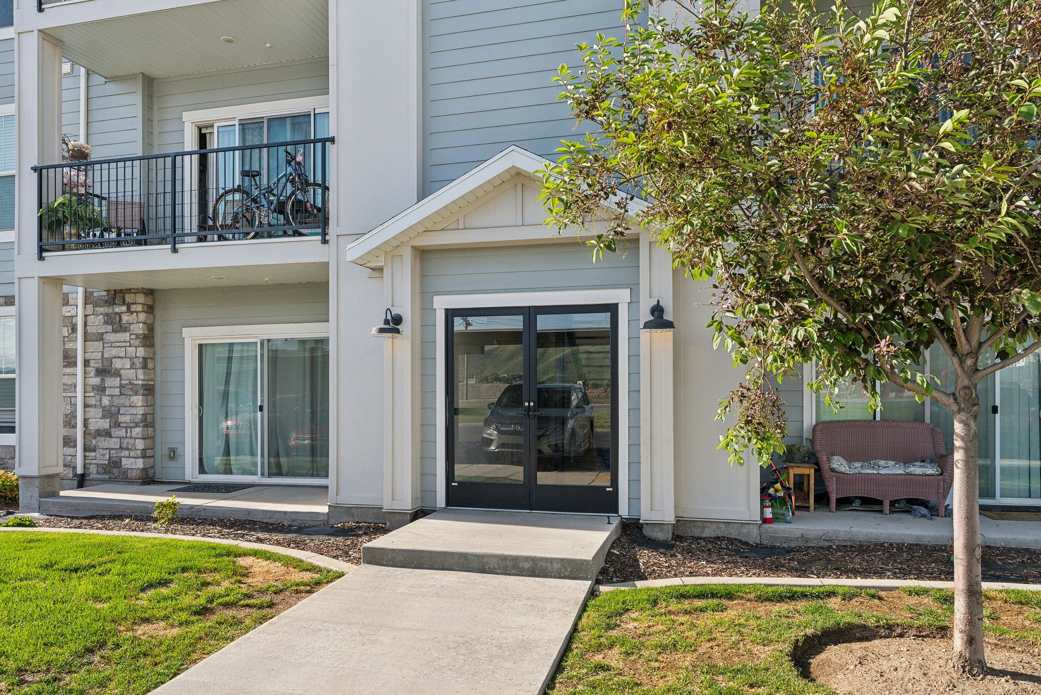 Exterior features include a covered entrance with double glass doors, light gray siding, and stone accent paneling