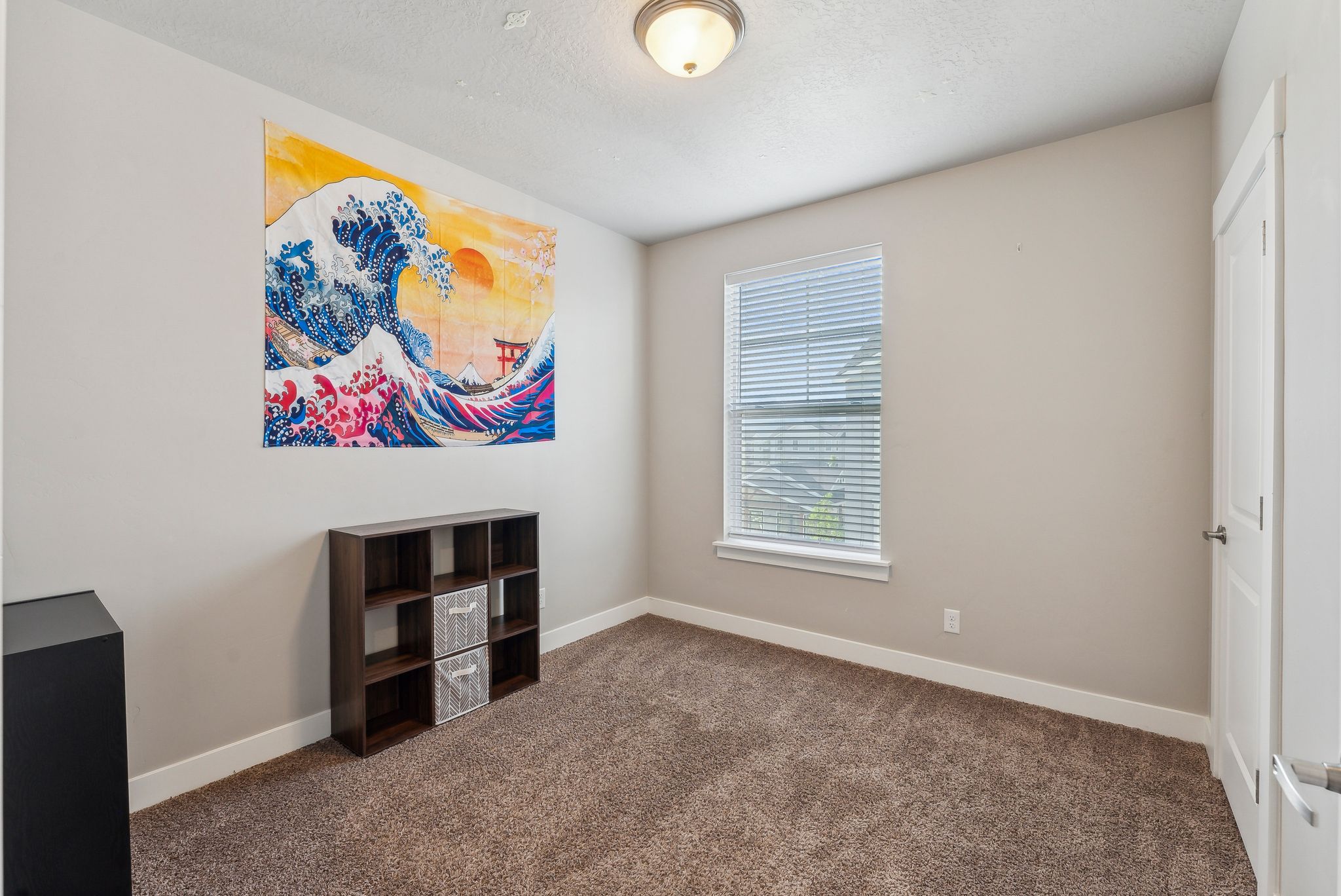 Neutral-toned wall paint with white trim, brown carpet flooring, and a single window with blinds