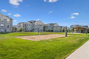 Sand volleyball court on a manicured lawn, surrounded by multi-story residential buildings featuring balconies and covered parking