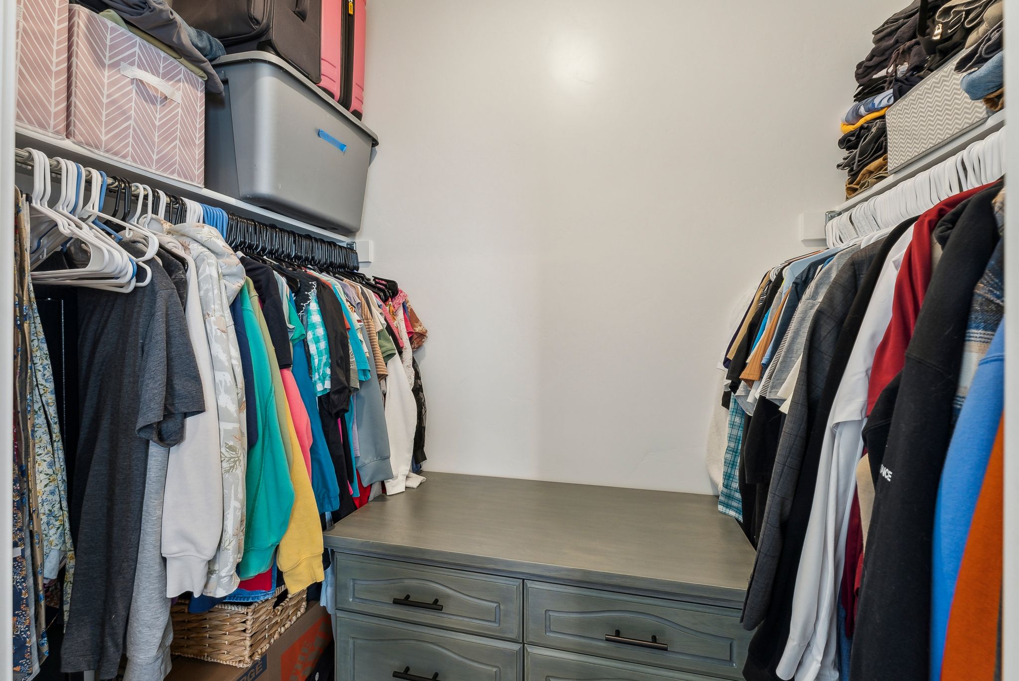 Walk-in closet featuring extensive shelving, dual hanging rods, and a central dresser unit with dark hardware