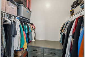 Walk-in closet featuring extensive shelving, dual hanging rods, and a central dresser unit with dark hardware