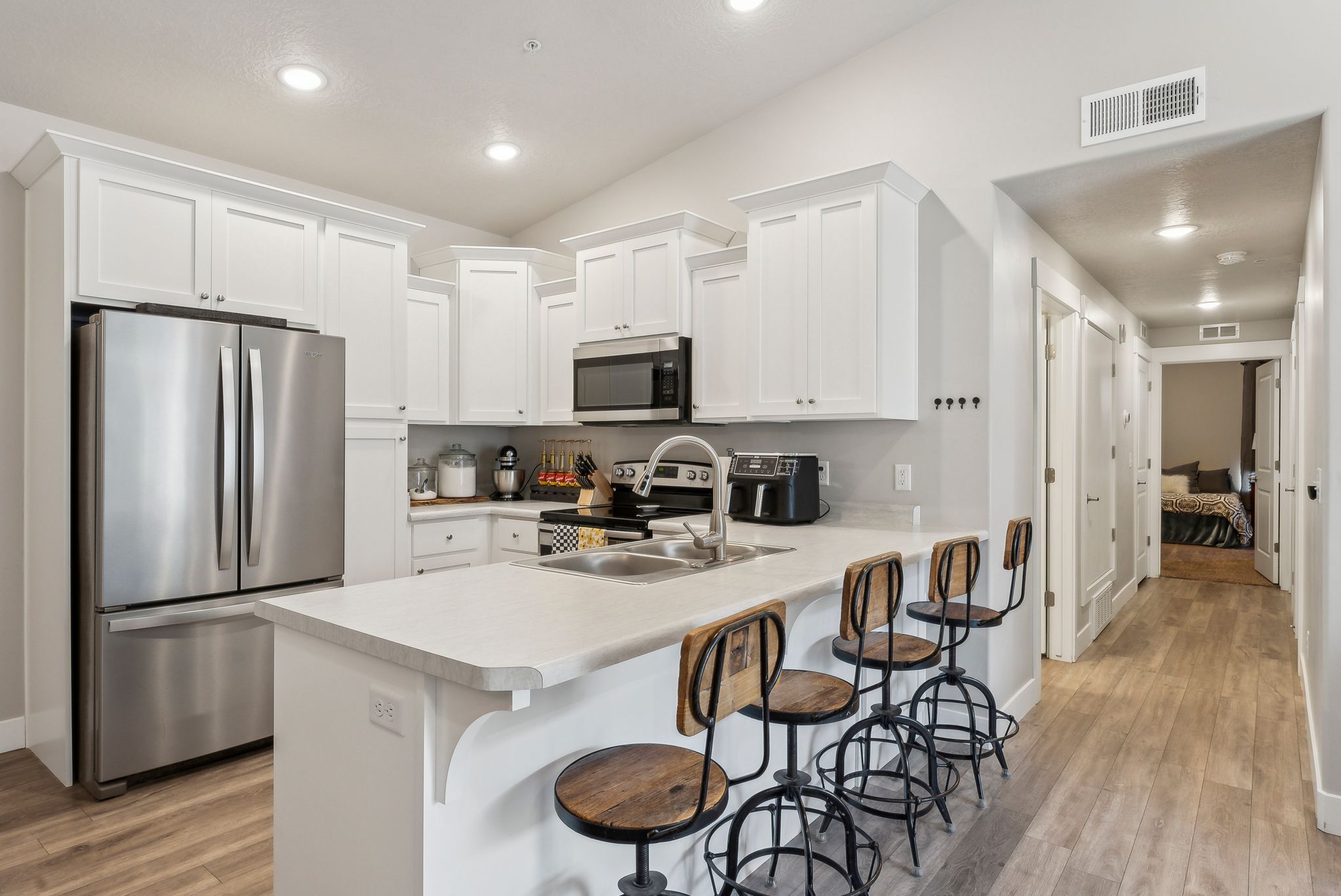 Modern kitchen featuring white shaker cabinetry, stainless steel appliances, a light-toned countertop, a double basin sink, and wood-finish flooring