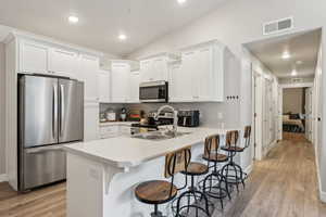 Modern kitchen featuring white shaker cabinetry, stainless steel appliances, a light-toned countertop, a double basin sink, and wood-finish flooring