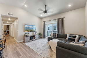Spacious living area featuring vaulted ceilings, recessed lighting, wood-finish flooring, and a sliding glass door leading to a balcony