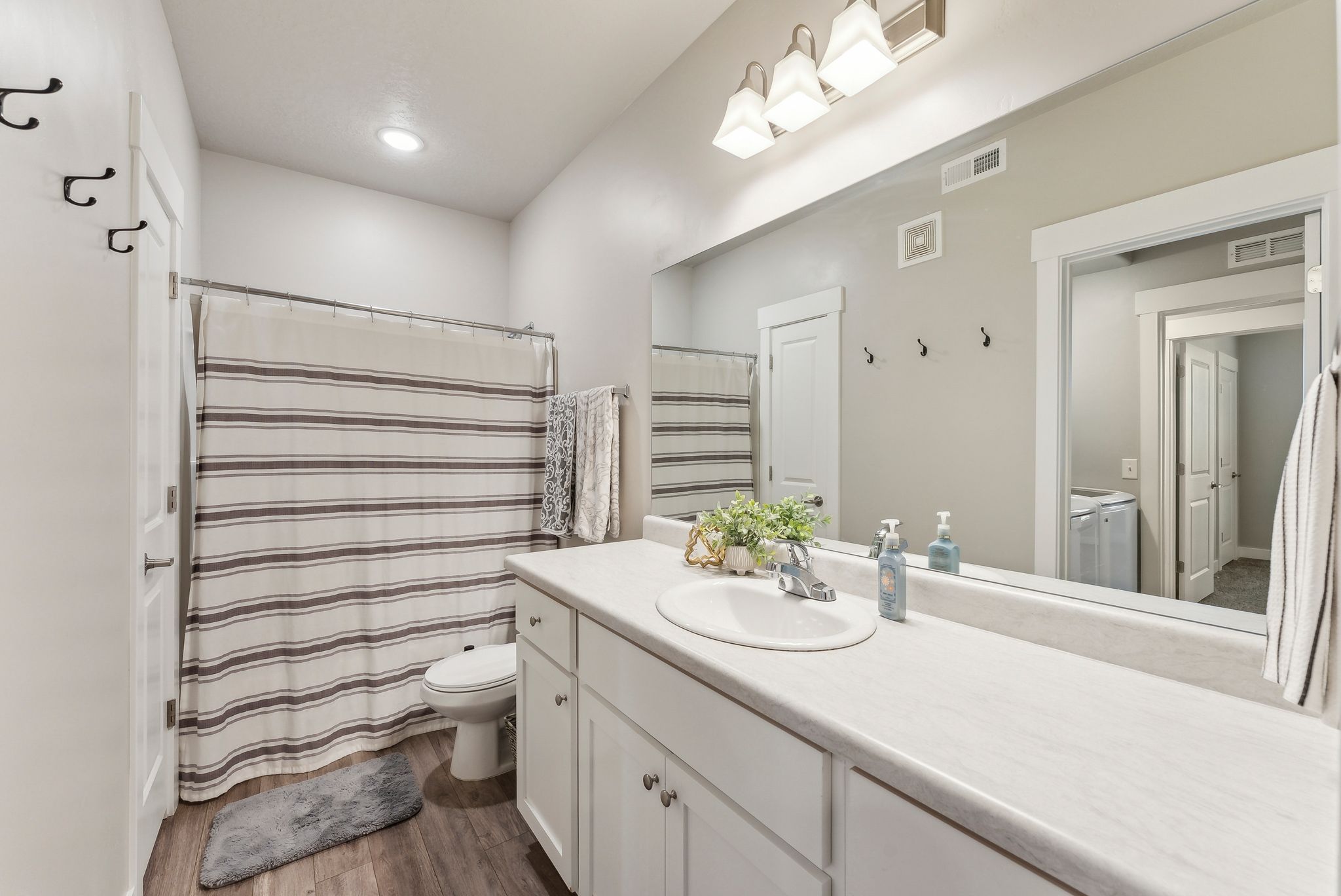 Bathroom featuring a single vanity with white cabinetry, a large mirror, and wood-finish flooring