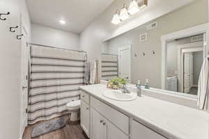 Bathroom featuring a single vanity with white cabinetry, a large mirror, and wood-finish flooring