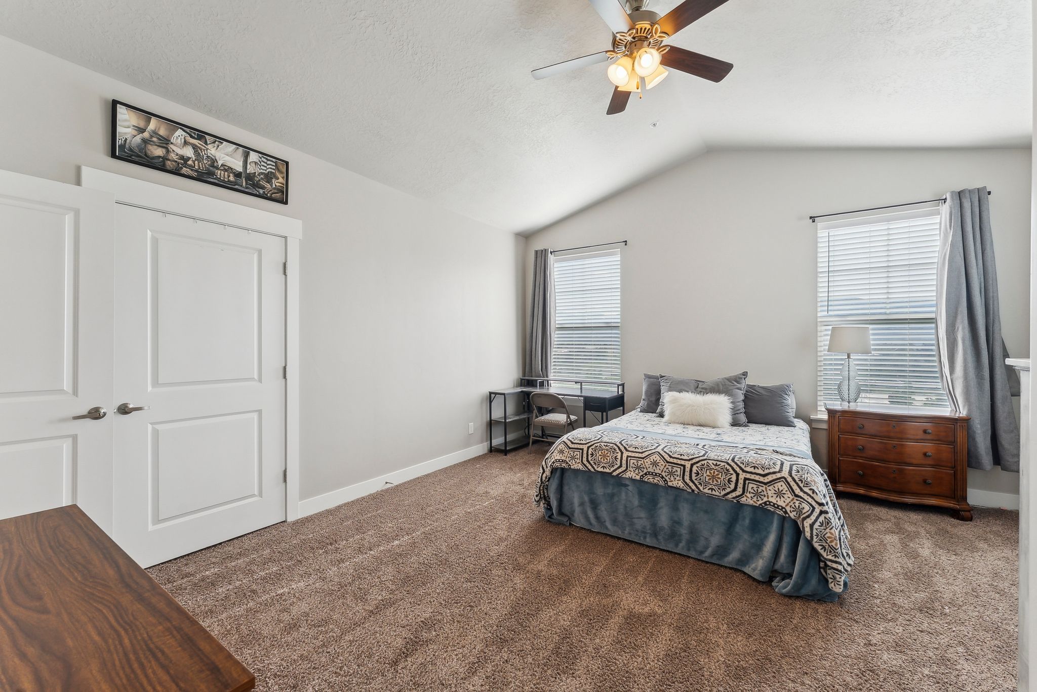 Vaulted ceiling bedroom featuring carpeting, a ceiling fan with integrated lighting, and two windows with blinds