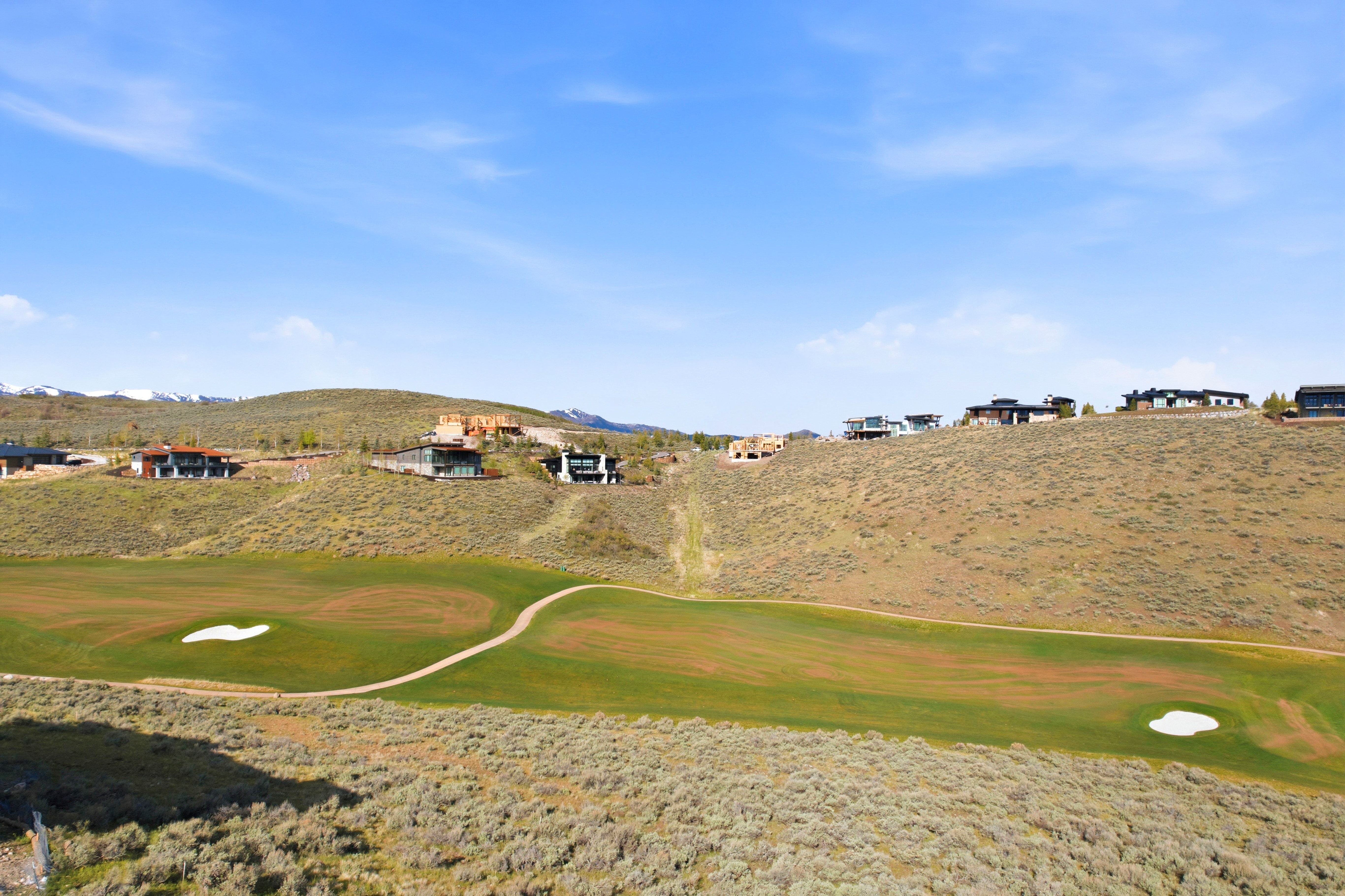Expansive golf course terrain featuring green fairways, sand traps, and a paved cart path
