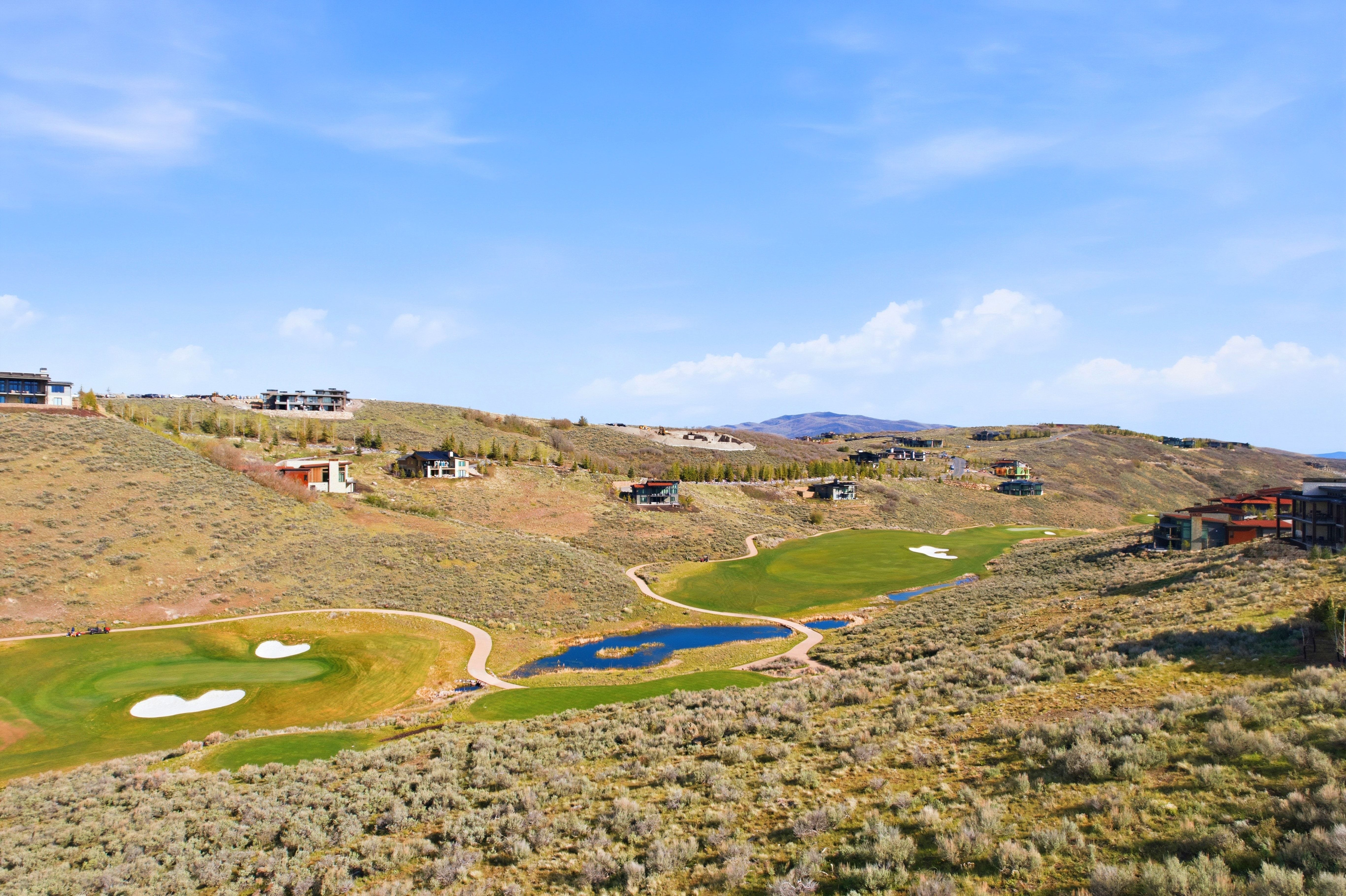 Expansive hillside property featuring a golf course, multiple greens, and a water feature
