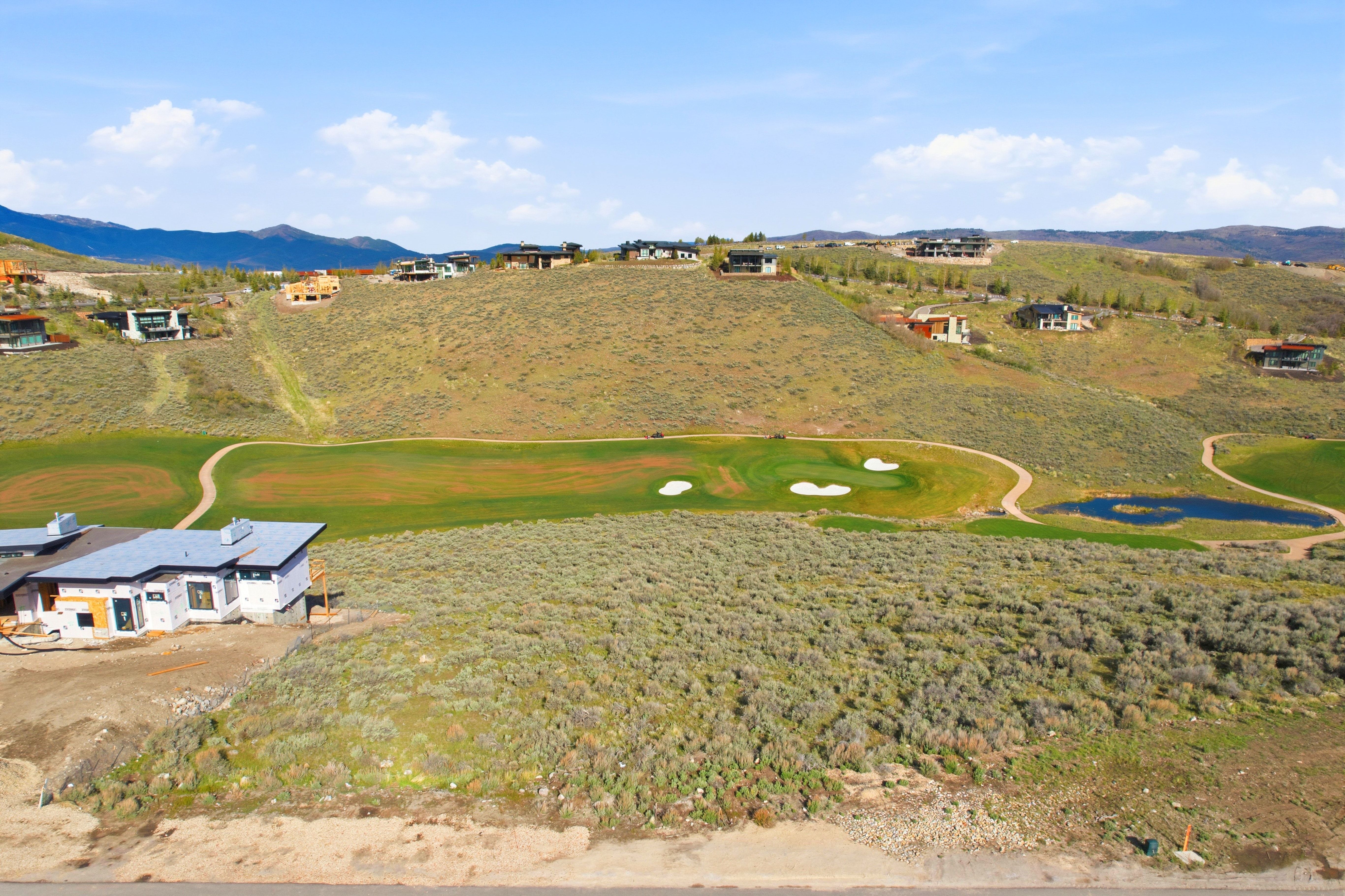 Expansive golf course property featuring a partially constructed residence, green fairways, and a water feature
