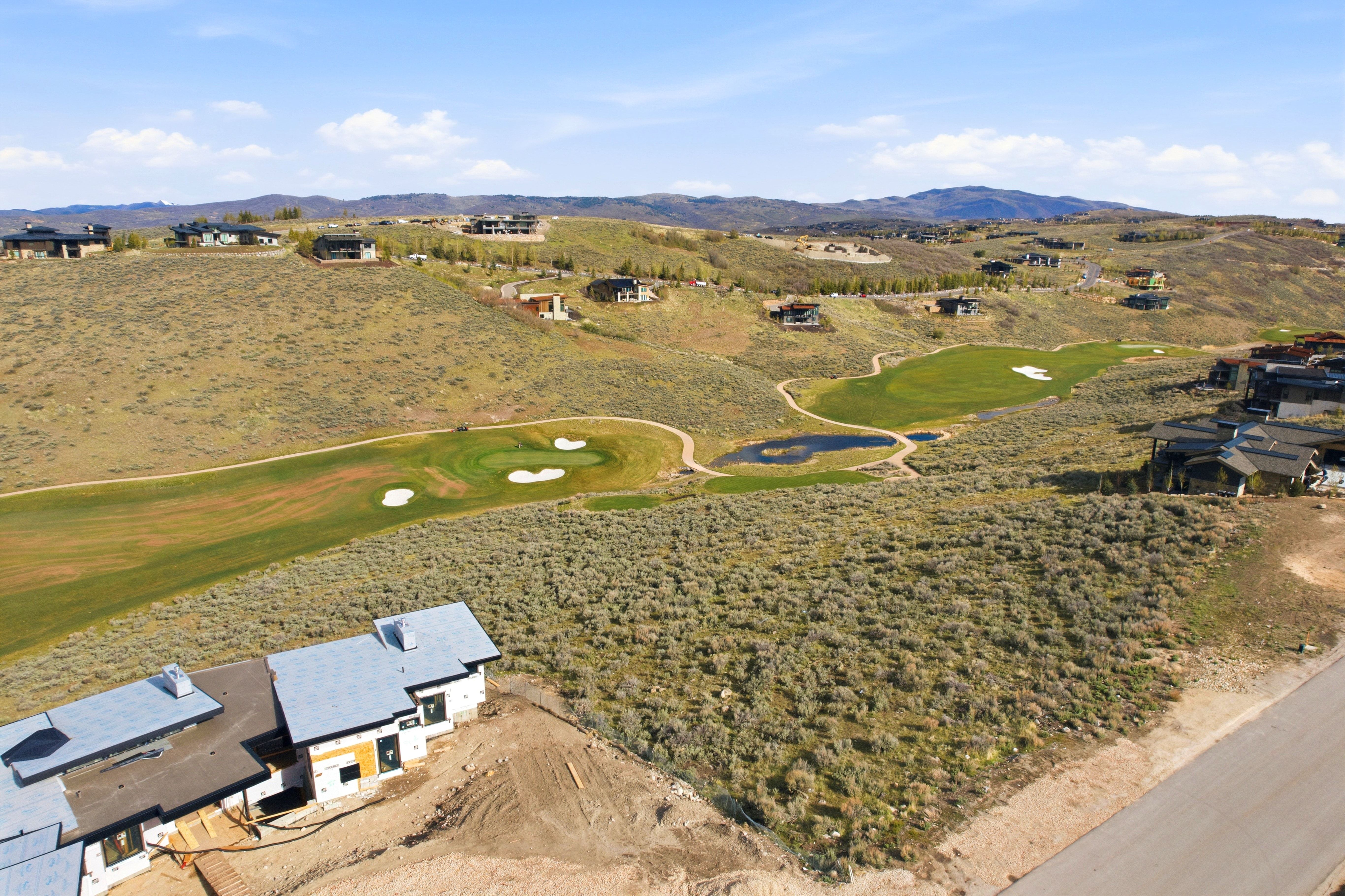Expansive undeveloped lot featuring natural vegetation, a paved road border, and a building under construction
