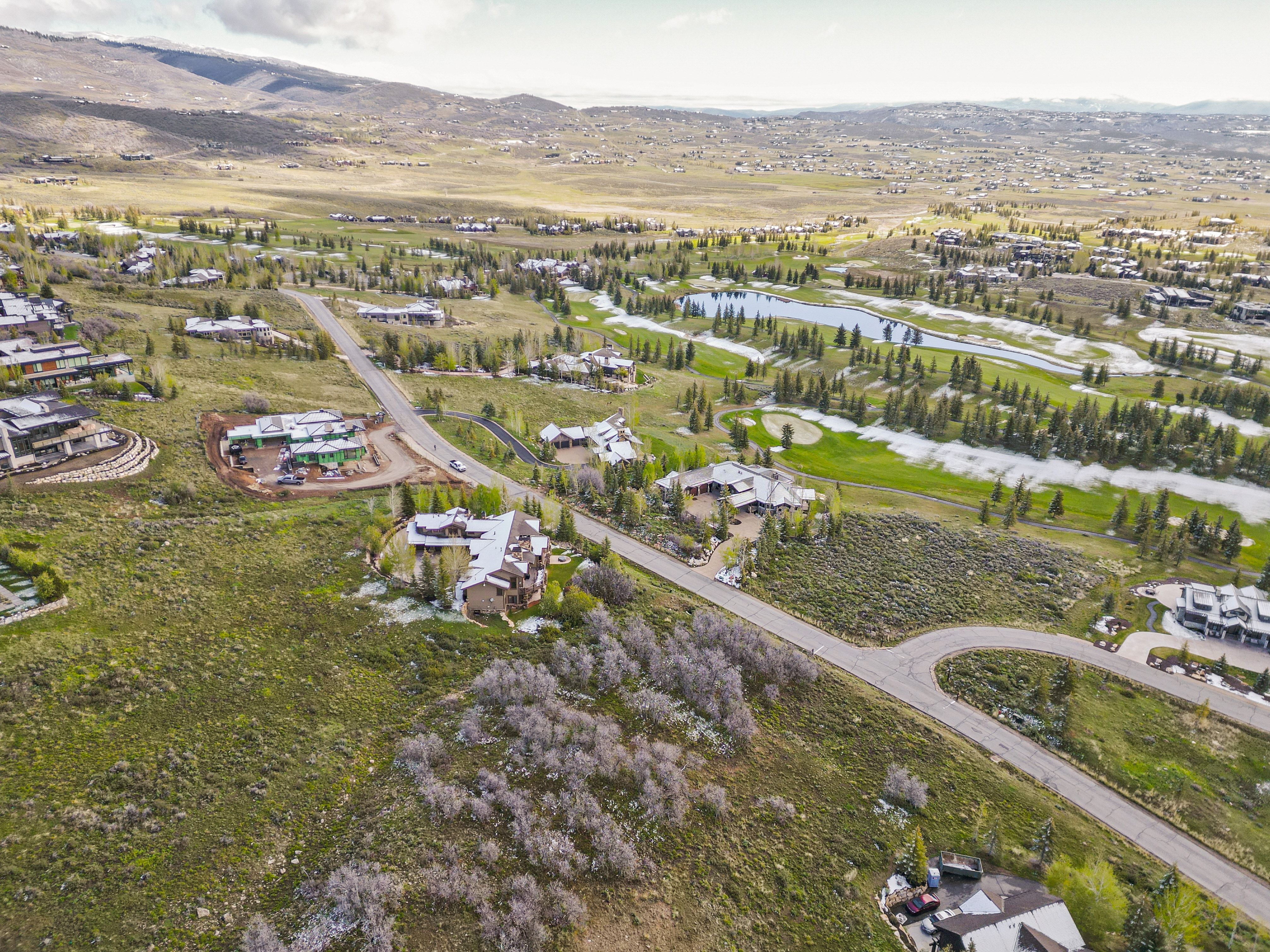 Expansive aerial depiction of a residential area featuring a golf course with water features, surrounding green spaces, and mountain backdrop