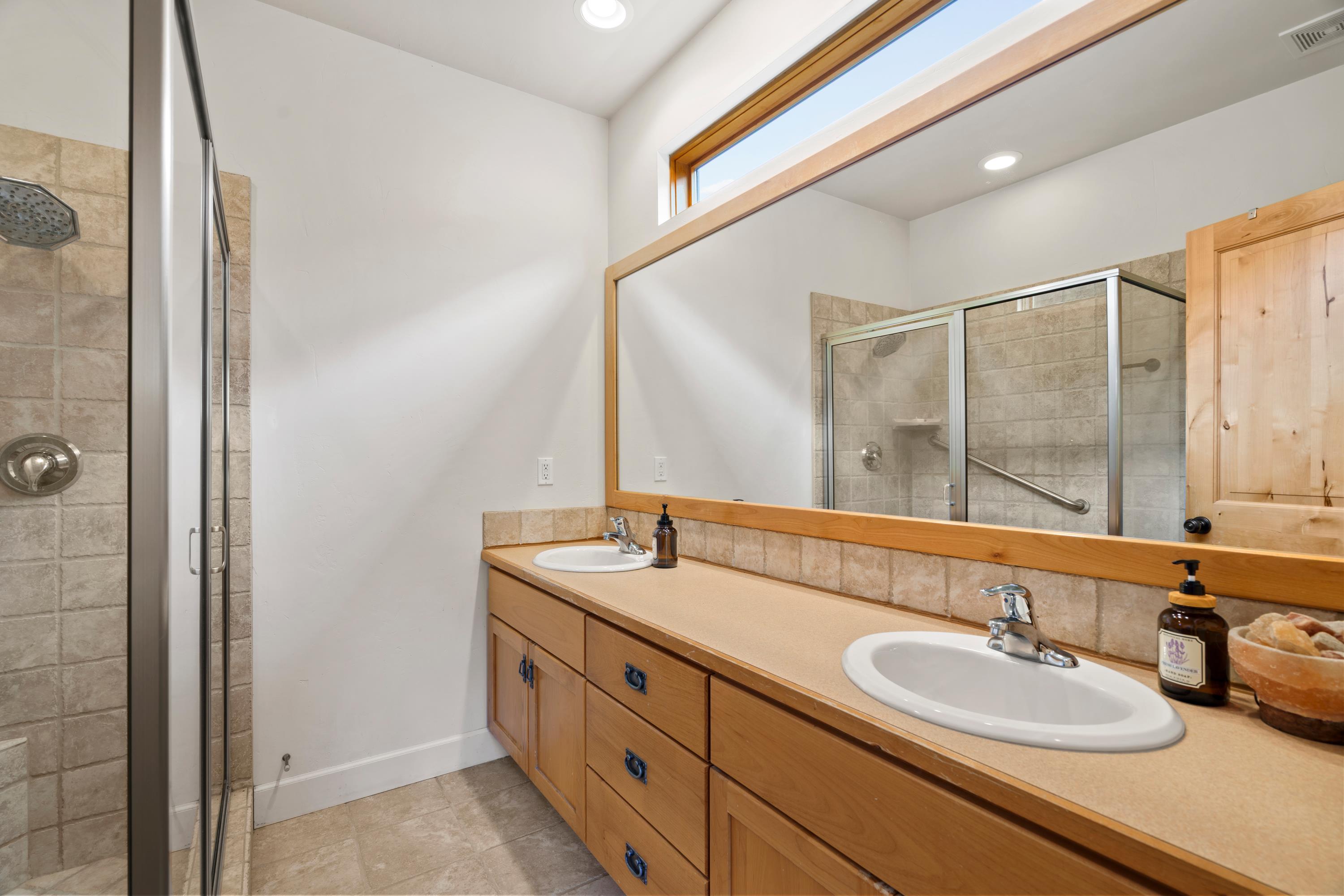 Bathroom featuring a double vanity with light wood cabinetry, dual undermount sinks, and a full-width mirror