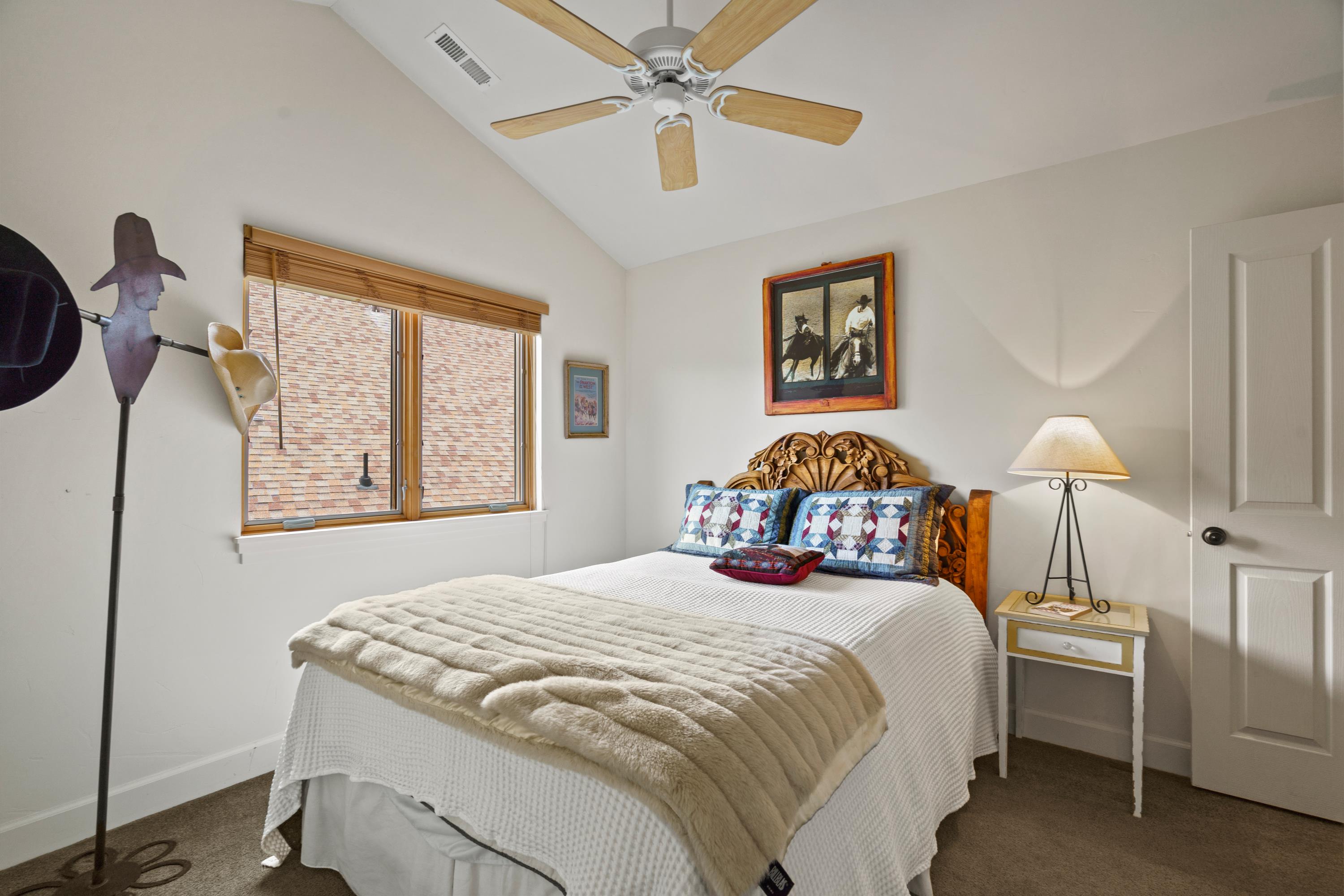 Vaulted ceiling bedroom with a wood-finish ceiling fan and two-panel interior door