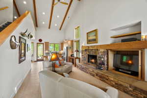Spacious living area featuring a vaulted ceiling with exposed wood beams, a stone fireplace, and a large built-in media cabinet