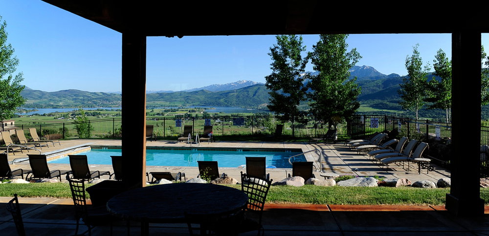Outdoor swimming pool with surrounding concrete decking, a grassy perimeter, and a distant mountain and lake backdrop