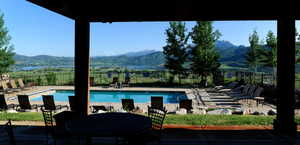 Outdoor swimming pool with surrounding concrete decking, a grassy perimeter, and a distant mountain and lake backdrop