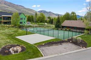 Outdoor sports court featuring a tennis court with black fencing and a concrete pad with a basketball hoop