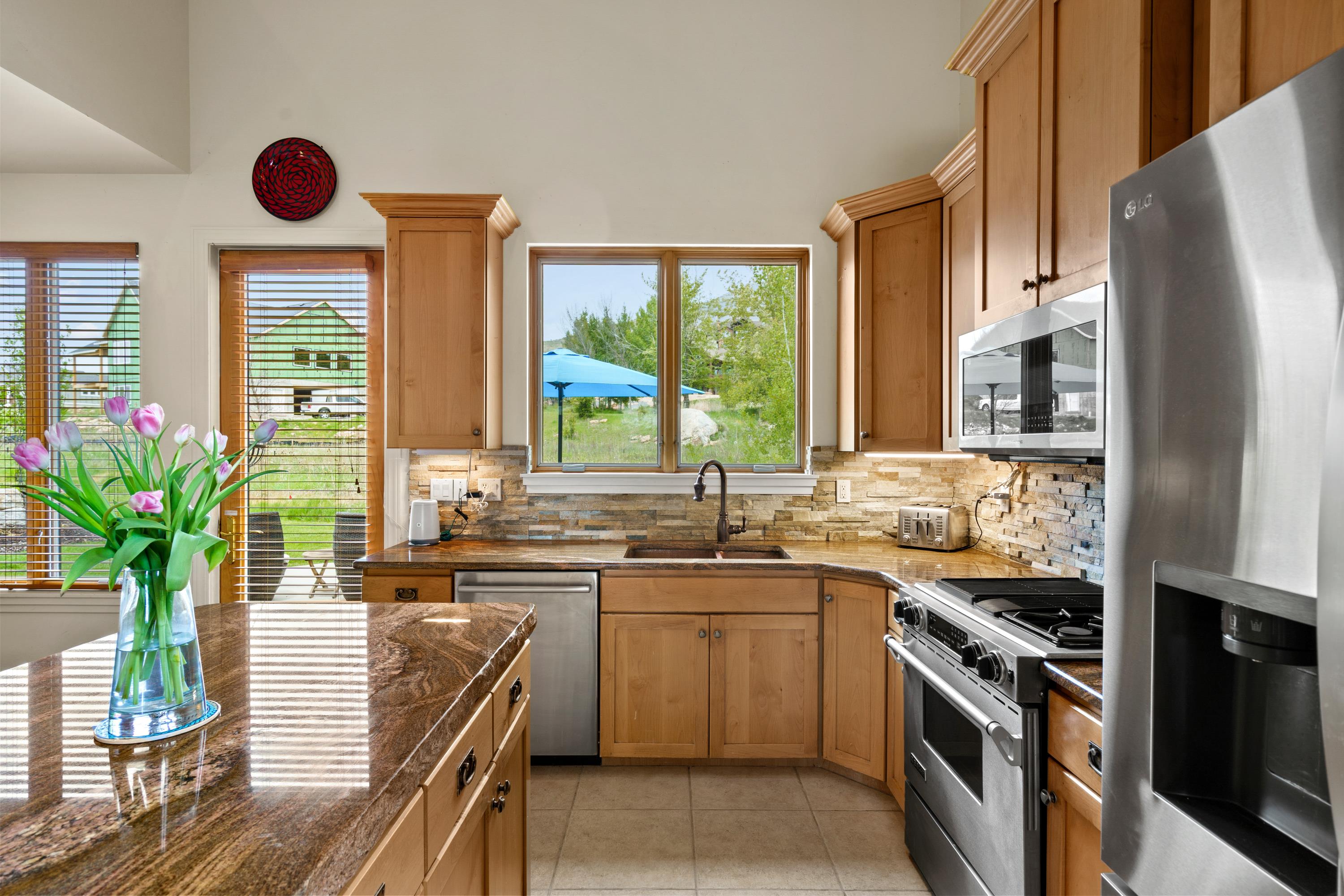 Kitchen featuring light wood cabinetry, stone-finish countertops, stainless steel appliances, and a stone-tile backsplash