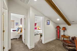 Carpeted hallway featuring vaulted ceilings, recessed lighting, and an exposed wood beam
