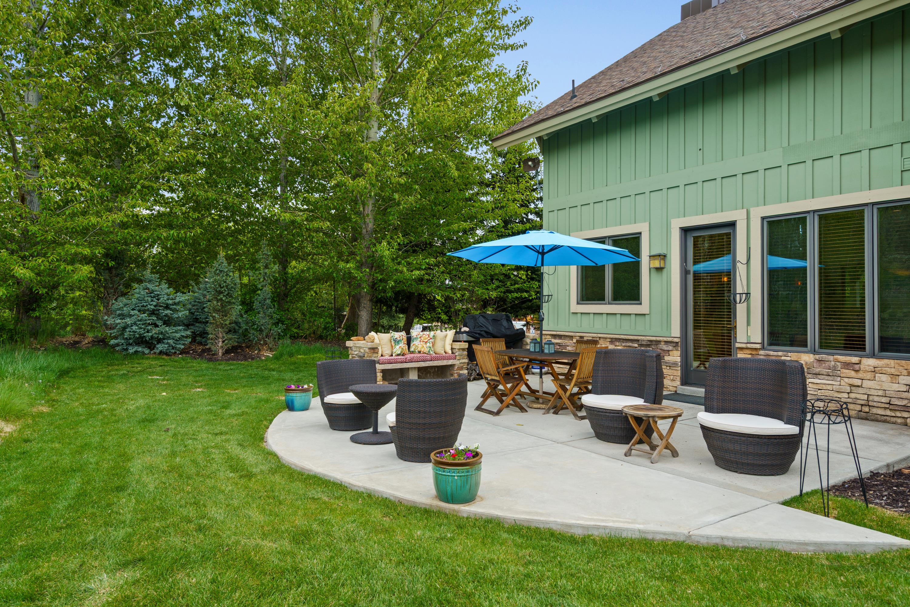 Spacious concrete patio with stone veneer siding, board and batten exterior, and mature trees providing natural screening