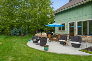 Spacious concrete patio with stone veneer siding, board and batten exterior, and mature trees providing natural screening